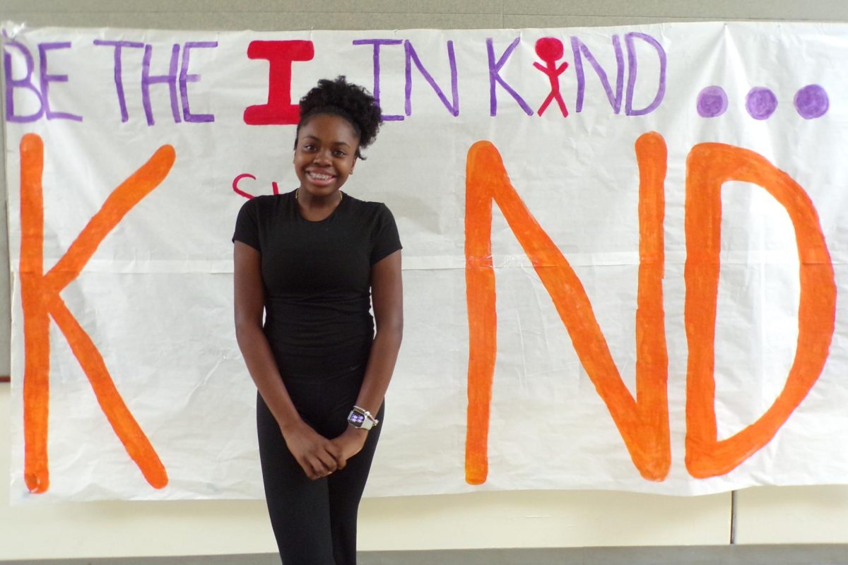 London Bell poses in front of the kindess poster. ASB leaders created this poster to remind students to take initiative to include others throughout the month of November.